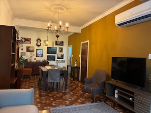 A living room with a television, a chandelier, and a dining area with chairs and a table. - Paulista | Entire apartment of 170 m², 3 bedrooms and parking space (São Paulo)
