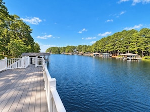 A wooden dock extending over calm water, surrounded by dense green trees. - ⛵ The Social House | Lake Gaston Waterfront, Dock, Porches, Arcade & Ping-Pong ☀ (Henrico)