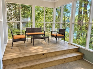 Eine überdachte Veranda mit Holzboden, einer Treppe und Korbmöbeln mit Kissen.