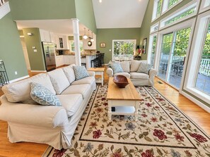 A spacious living room with a sofa set, a coffee table, and a view of the kitchen and outdoor patio. - ⛵ The Social House | Lake Gaston Waterfront, Dock, Porches, Arcade & Ping-Pong ☀ (Henrico)