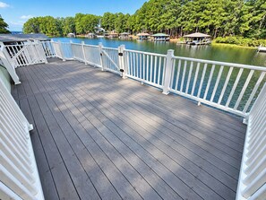 Une terrasse en bois avec des rampes blanches donnant sur une étendue d’eau, entourée d’arbres.