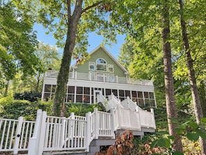 Une maison à deux étages avec un balcon, entourée d’arbres.