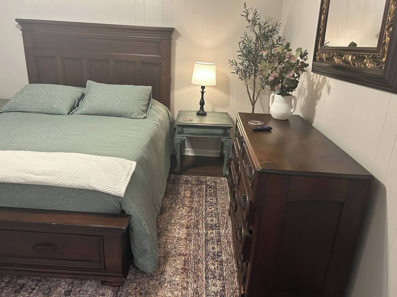 A bedroom with a bed, nightstands, a dresser, a lamp, and a mirror.