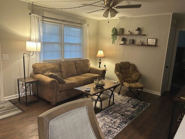 A living room with a sofa, armchair, coffee table, and a ceiling fan.