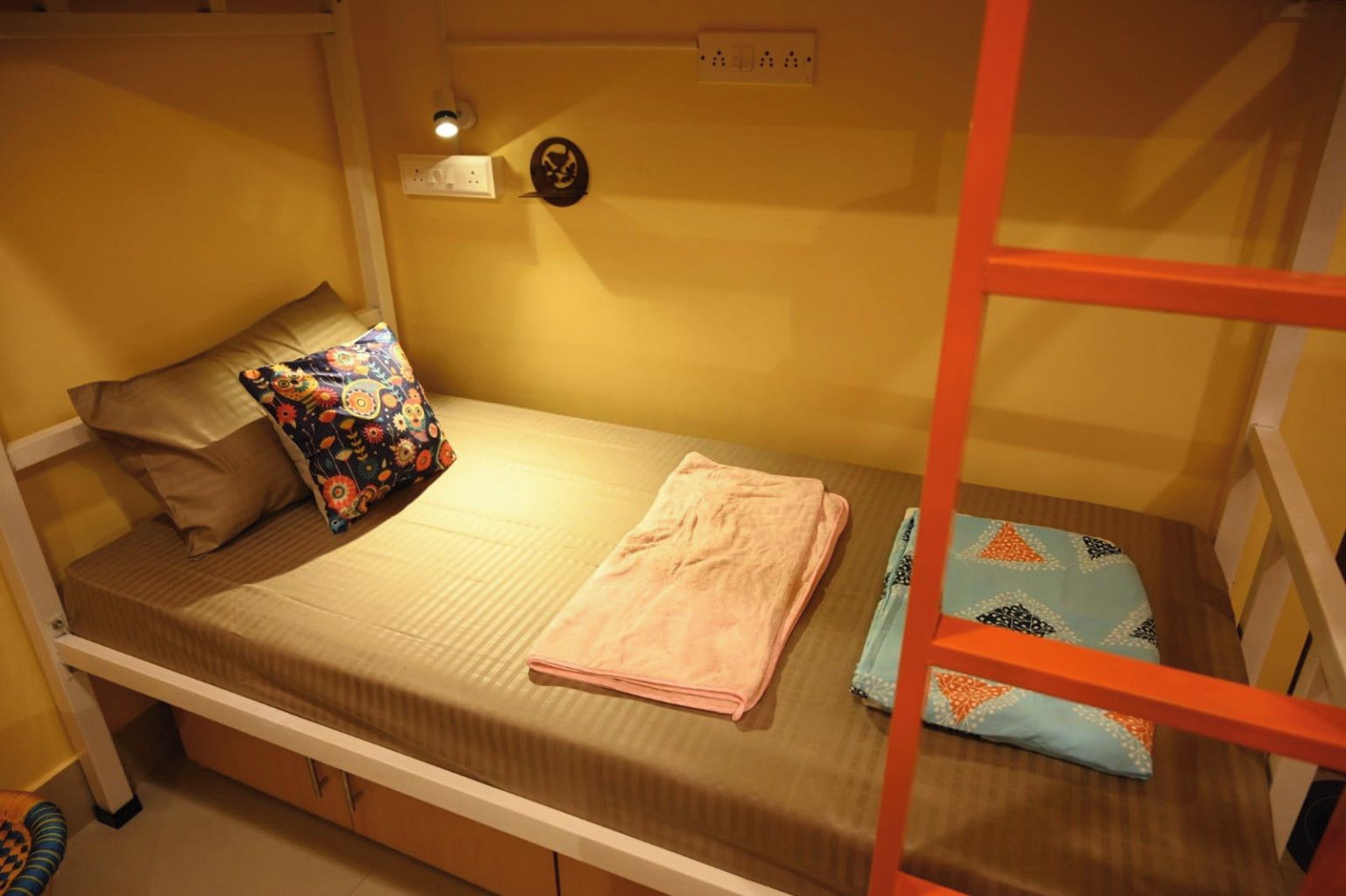 A bunk bed with a single bed on top and a lower bunk. There is a pillow with a floral pattern on the single bed, a folded pink towel on the lower bunk, and a blue patterned pillow on the lower bed.