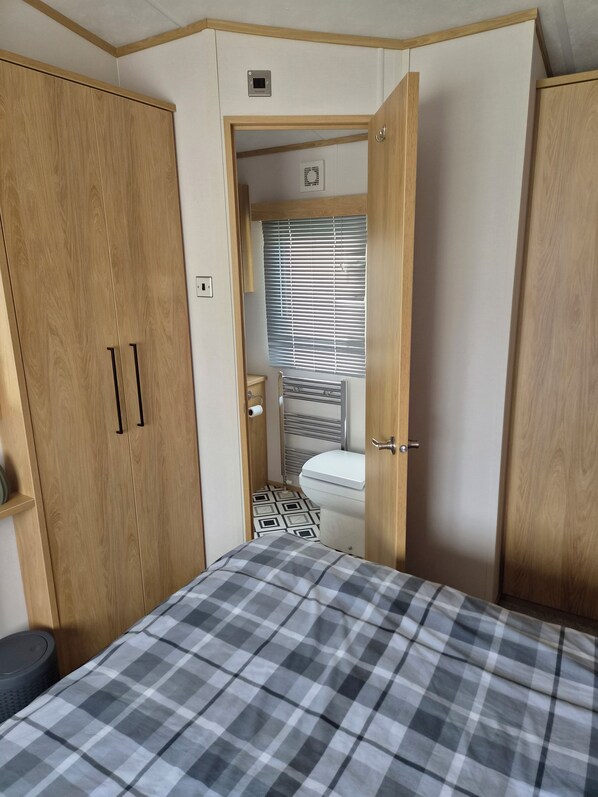 A bedroom with a bed, wooden wardrobe, and a bathroom visible through an open door.