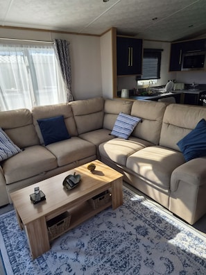 A living room with a beige sectional sofa, a wooden coffee table, and a patterned rug. - Luxury Sea View Lodge (Southerness)