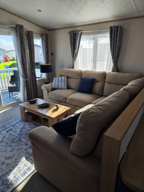 A modern living room with a sofa, a coffee table, and a lamp. There is a view of the outside through large windows.