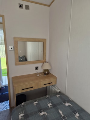 A bedroom with a bed, a bedside table with a lamp, a mirror, and a radiator. - Luxury Sea View Lodge (Southerness)