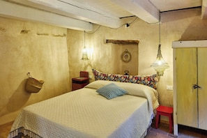 A bedroom with a bed, a nightstand, a hanging lamp, a wall-mounted shelf, and a door. - Apartment in a stone mill with panoramic view (Mombaroccio)