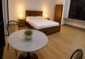 Una camera da letto con un letto, comodini, un armadio, un tavolo rotondo con una pianta in vaso e una sedia.