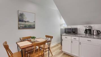 A modern kitchen with white cabinets, a microwave, a coffee maker, and a dining area with a wooden table and chairs.
