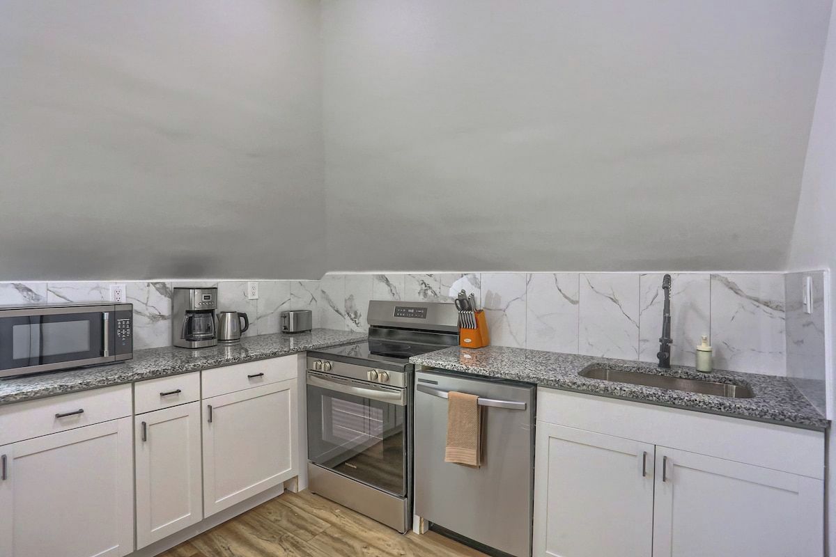 A kitchen with white cabinets, a stainless steel oven, a microwave, a coffee maker, and a sink.