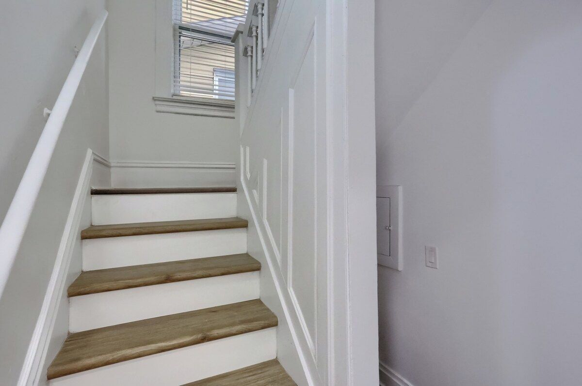 A staircase with wooden steps and white walls, leading to a room with a window.