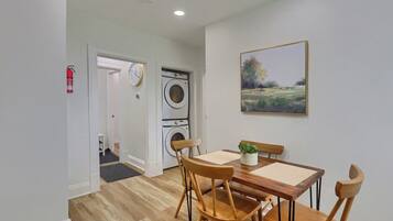 A dining area with a table and chairs, a washing machine, a fire extinguisher, and a clock on the wall.