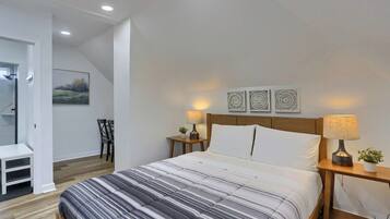 A bedroom with a bed, two bedside tables, a nightstand, a chair, a small table, and a painting on the wall.