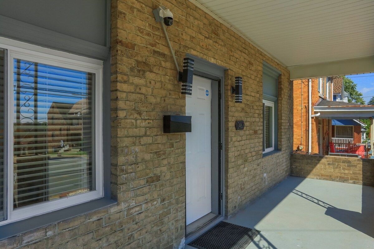 A brick building with a white door, a security camera, and a covered outdoor area.