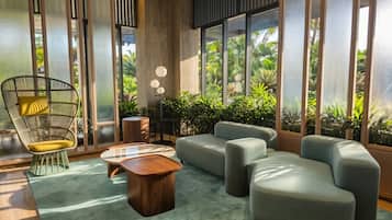Een moderne woonkamer met een bank, een fauteuil, een salontafel en een vloerlamp. Grote ramen bieden uitzicht op groen buiten.