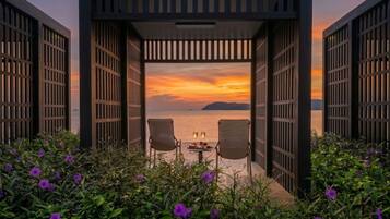 Een open constructie met twee stoelen gericht op een uitzicht op het water tijdens zonsondergang.