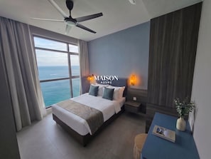 Quarto de hotel com cama, mesas de cabeceira, escrivaninha e vista para o mar.