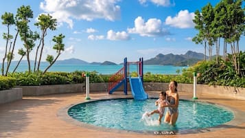 Una piscina con tobogán, rodeada de palmeras y vistas al mar.