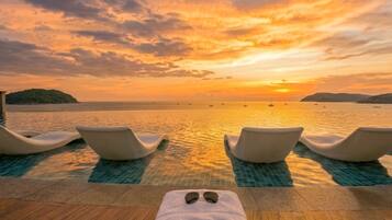 Oceanfront infinity pool with in-water loungers at golden sunset