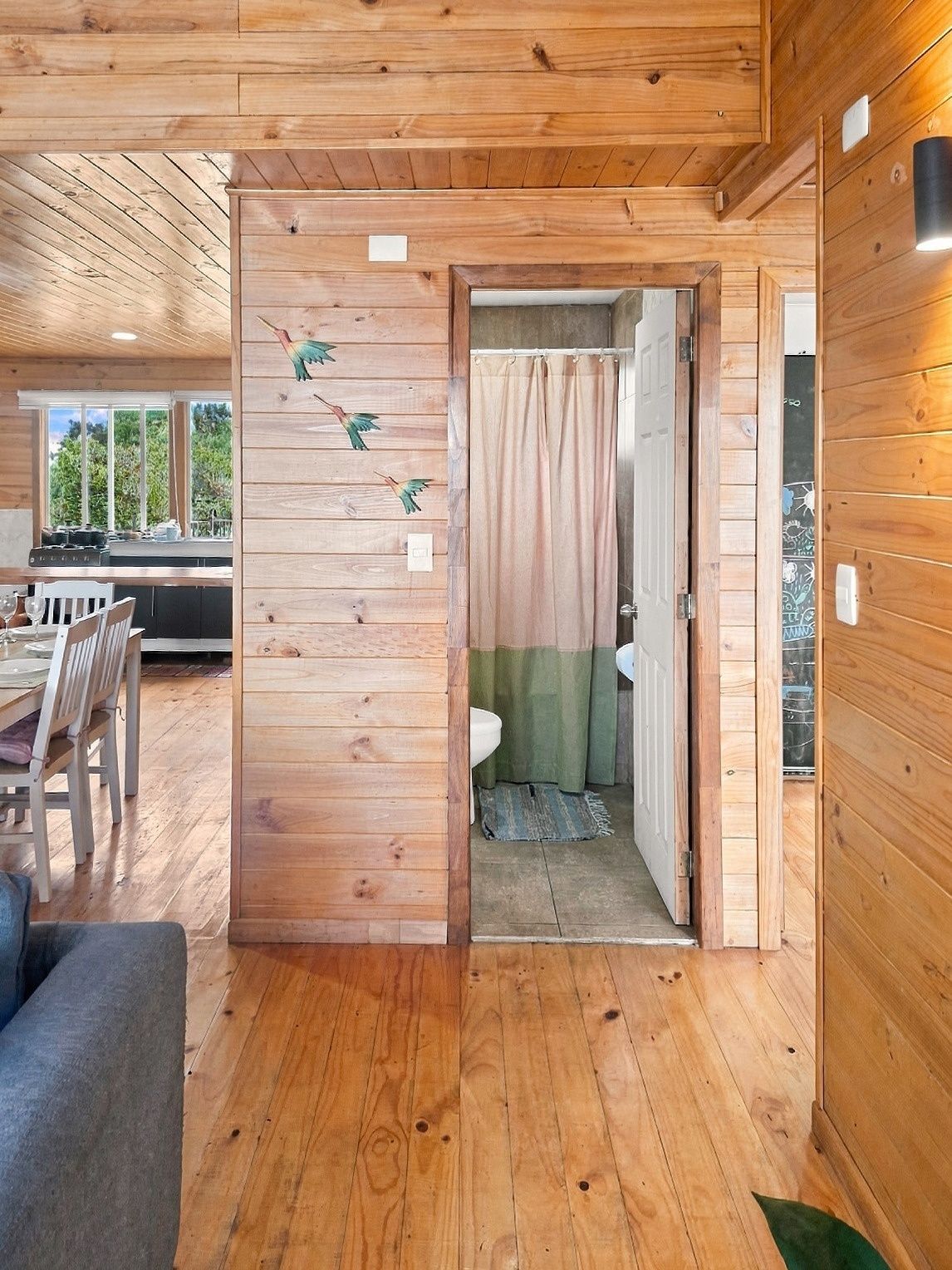 Een houten interieur met een eethoek, een badkamer met douchegordijn, en een zichtbaar raam.