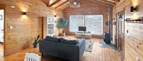 A spacious wooden interior with a high ceiling, a sofa, a television, and a fireplace.