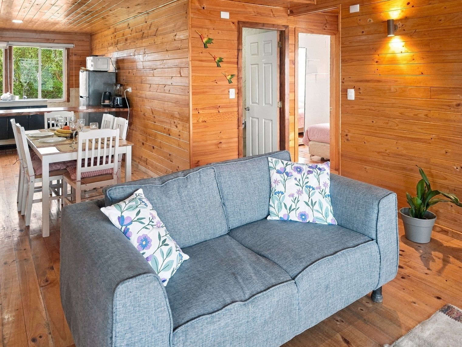 L’intérieur chaleureux d’un chalet avec un canapé gris, des murs en bois, un coin repas et une petite cuisine.