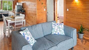 A cozy cabin interior with a grey sofa, wooden walls, a dining area, and a small kitchen.