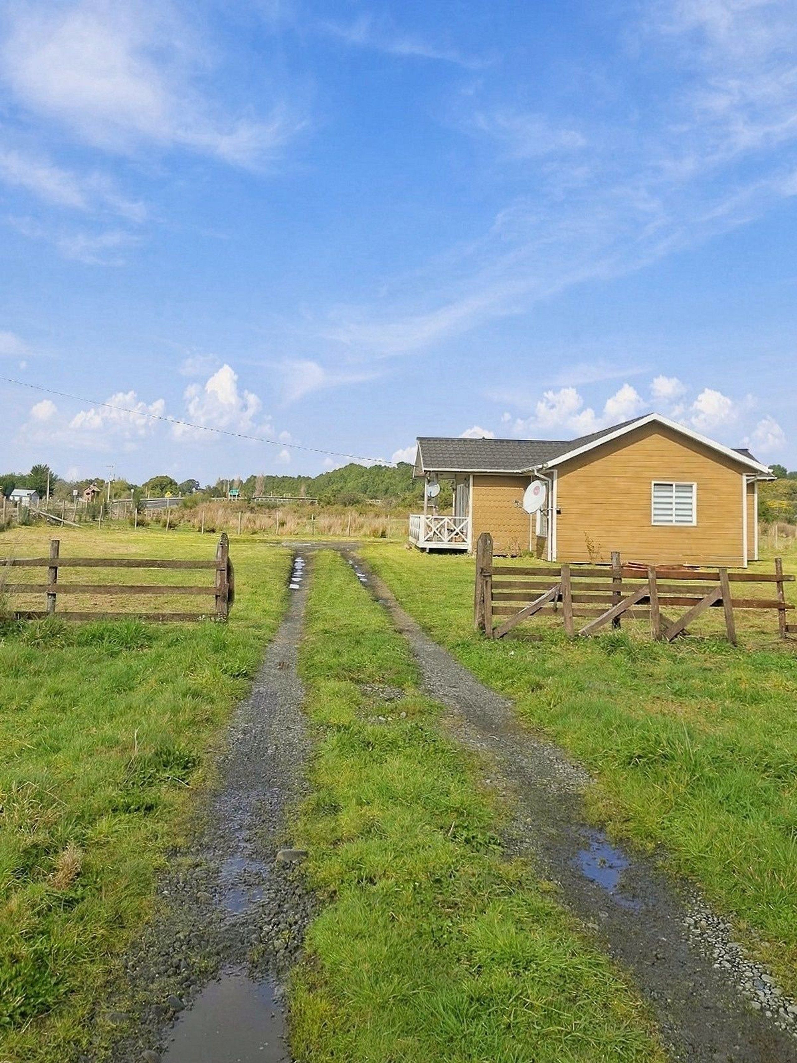 Propiedad rural con un camino de grava que conduce a una edificación de madera con patio cercado.
