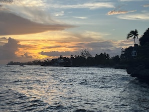 A coastal sunset with calm waters, a silhouette of palm trees, and buildings along the shore. - Sunset Beach Unit 10 St Lawrence Gap Condos (Oistins)