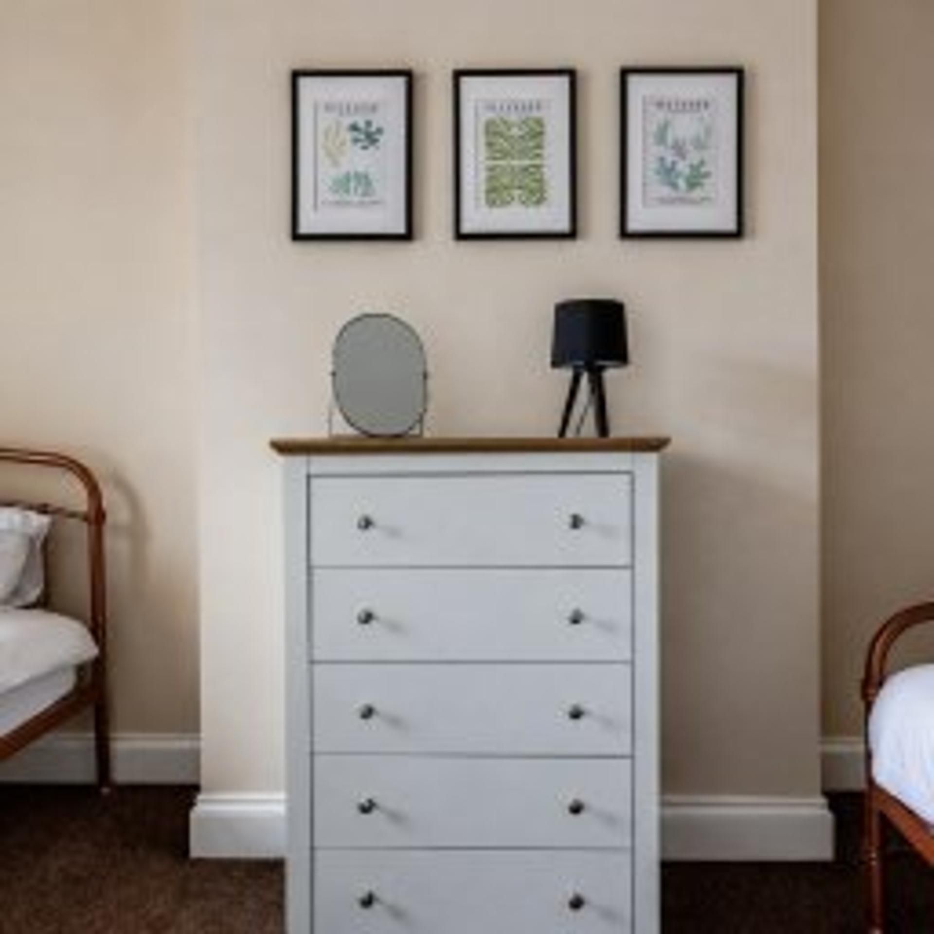 Une chambre à coucher comprenant un lit, une commode et trois reproductions botaniques encadrées accrochées au mur.