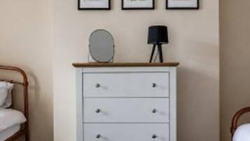 Une chambre à coucher comprenant un lit, une commode et trois reproductions botaniques encadrées accrochées au mur.