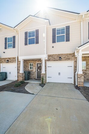 A two-story house with a garage, a brick facade, and a welcome sign. - Discovery Landing • Huntsville 3BR Townhome, Patio (Huntsville)