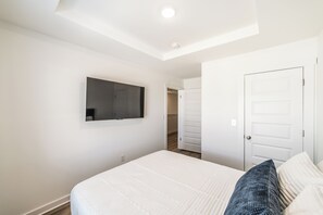 A bedroom with a bed, a flat-screen TV mounted on the wall, a closet with sliding doors, and a ceiling light. - Discovery Landing • Huntsville 3BR Townhome, Patio (Huntsville)