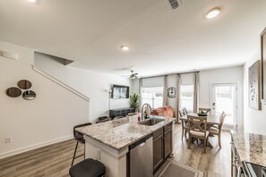A modern kitchen with a central island, a dining area with a table and chairs, and a staircase leading to another level. - Discovery Landing • Huntsville 3BR Townhome, Patio (Huntsville)