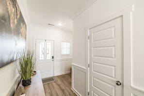 A hallway with a white door, a potted plant, and a wall-mounted artwork. - Discovery Landing • Huntsville 3BR Townhome, Patio (Huntsville)