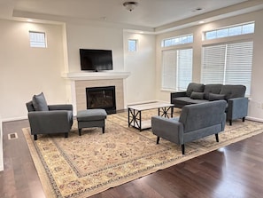 A living room with a fireplace, a flat-screen TV, and a large window with blinds. - Spacious 5-Bedroom House Near Park & Golf Course (Denver)