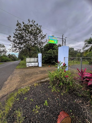 A rural road with a sign for Villa Zunzun, a coconut plantation sign, and a blue structure with a fence. - NEW! Cozy 1-bedroom bungalow in peaceful Chachagua with AC (San Ramon)