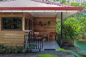 Una cabaña de madera con techo rojo, un porche con banca y una pequeña mesa.