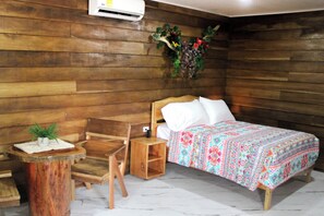 A wooden room with a bed, a chair, a small table, and an air conditioning unit on the wall. - NEW! Cozy 1-bedroom bungalow in peaceful Chachagua with AC (San Ramon)