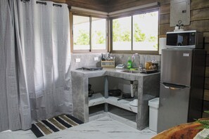 A compact kitchen with a refrigerator, microwave, and a window with a view of greenery. - NEW! Cozy 1-bedroom bungalow in peaceful Chachagua with AC (San Ramon)