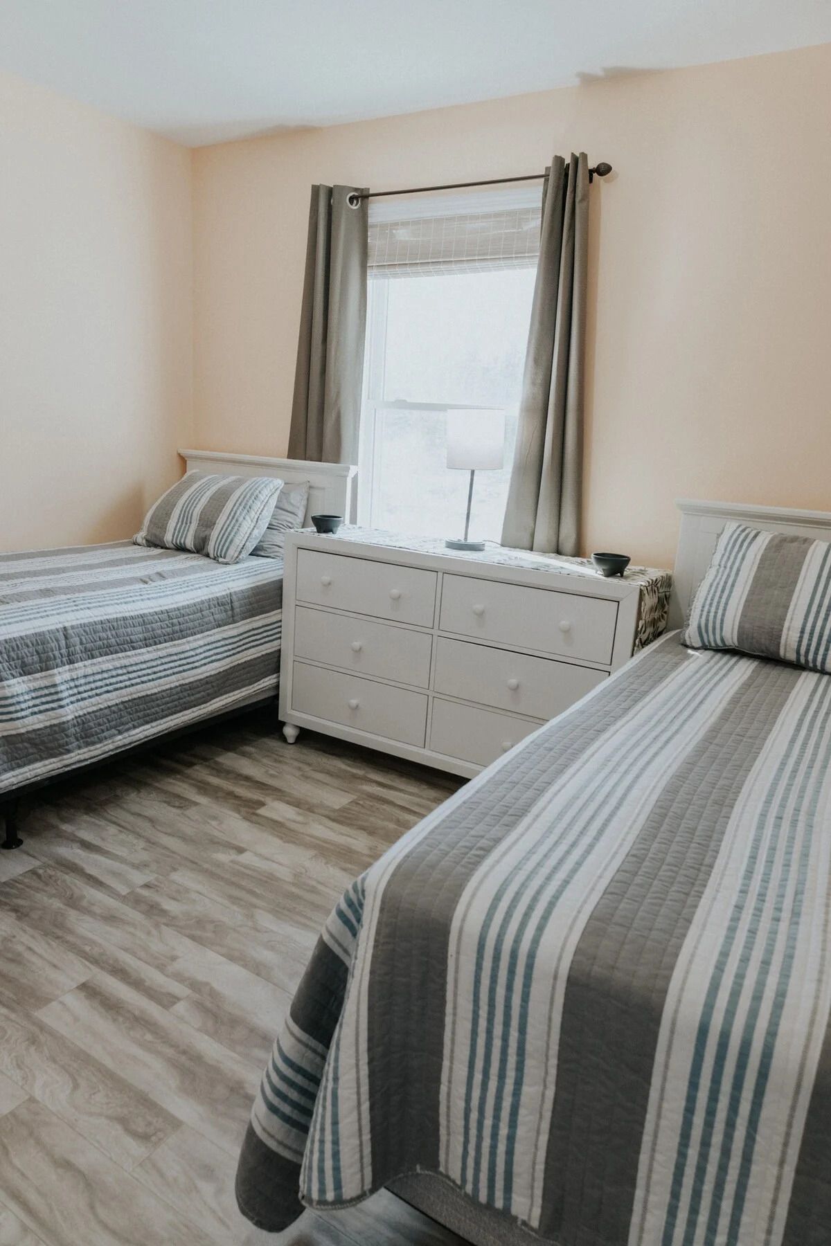 A bedroom with two beds, a dresser, and a window with curtains.