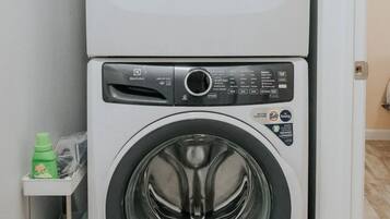 Lavadora y secadora apiladas en una habitación con piso de baldosas y una puerta al fondo.