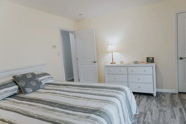 Un dormitorio con cama, mesita de noche, lámpara y puerta.