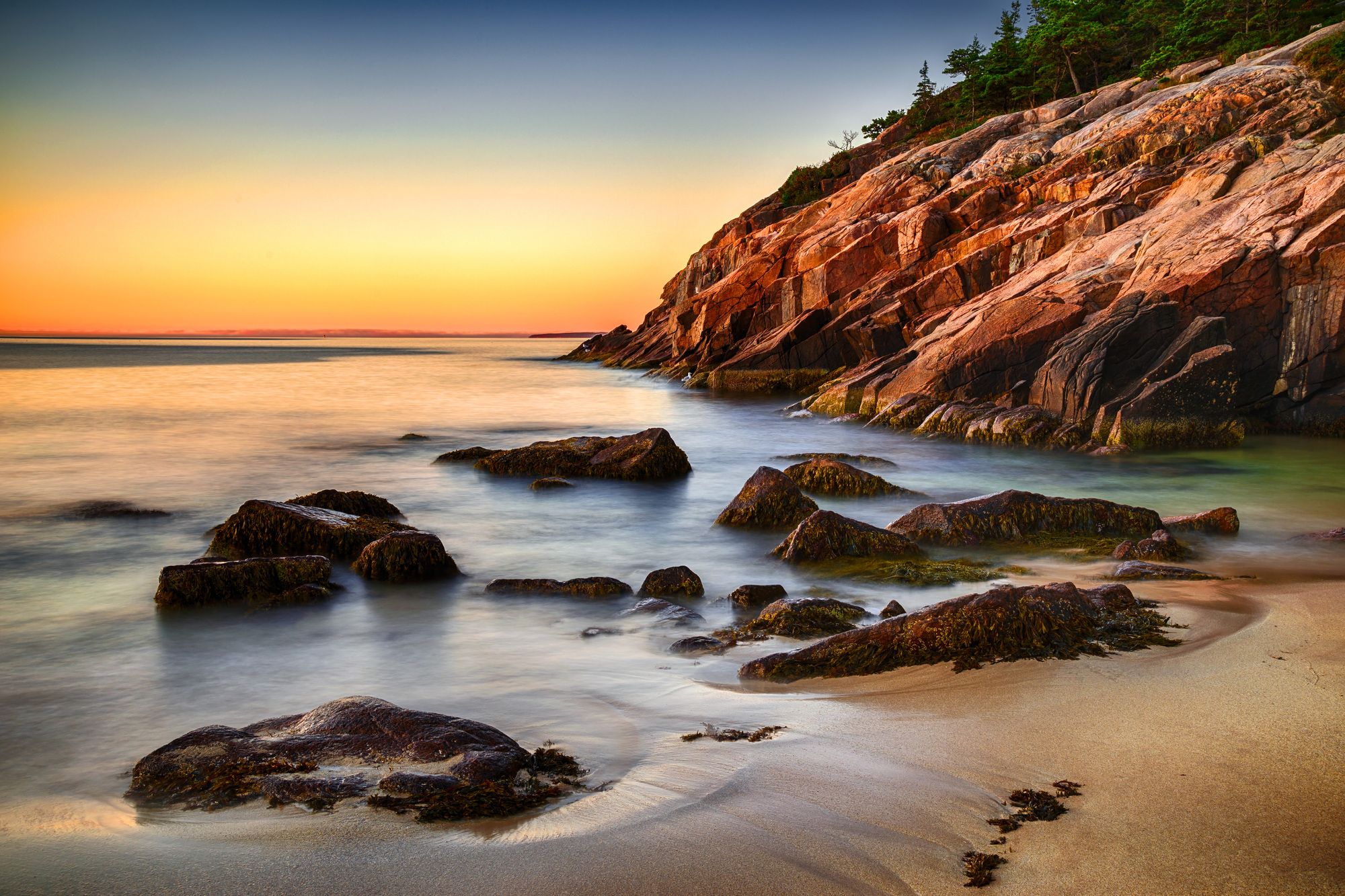 A coastal landscape with rocky formations, calm water, and a sandy beach.