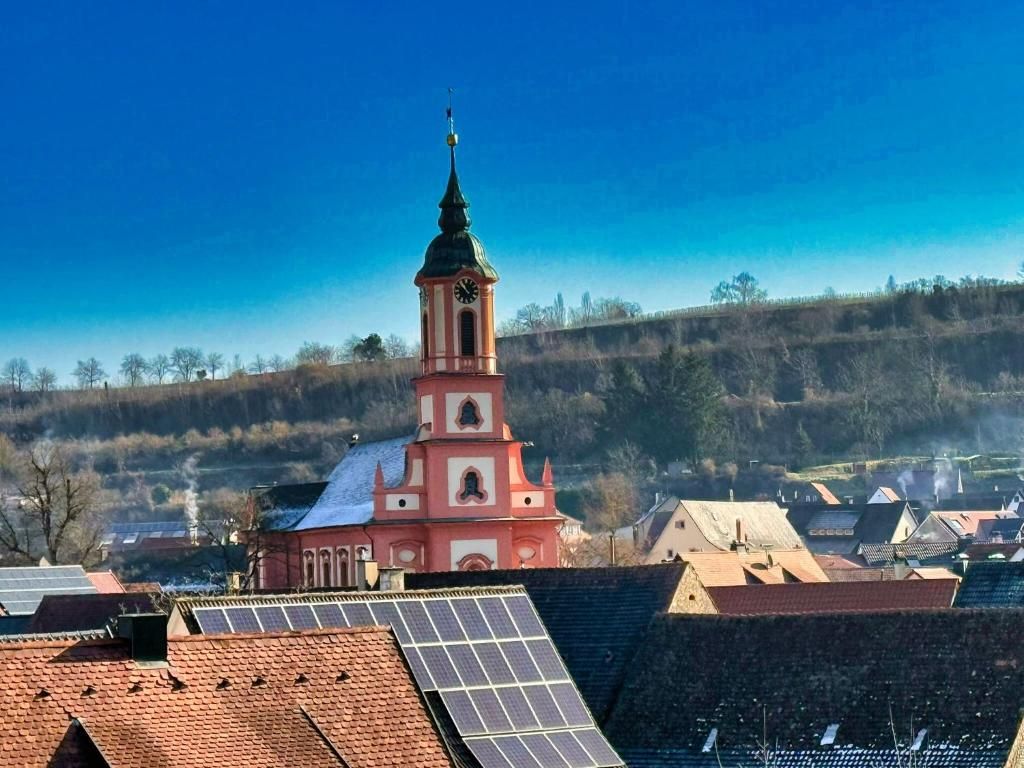 A church with a bell tower, surrounded by residential buildings and solar panels on rooftops.