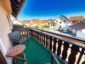 Un balcon doté d’un sol recouvert d’herbe, de meubles en osier et offrant une vue sur les maisons voisines.