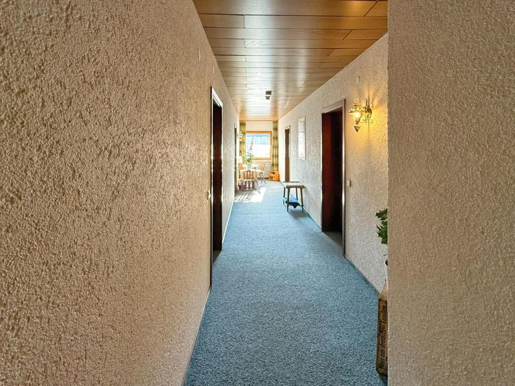 A corridor with a wooden ceiling, carpeted floor, and a dining area in the distance.